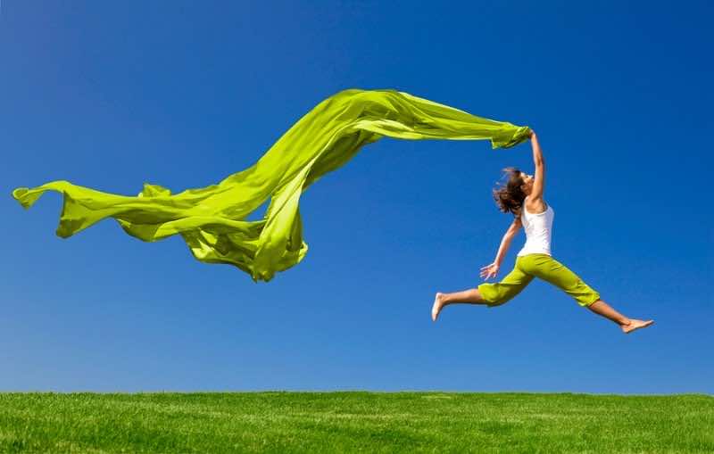 Beautiful young woman jumping on  a green meadow with a colored