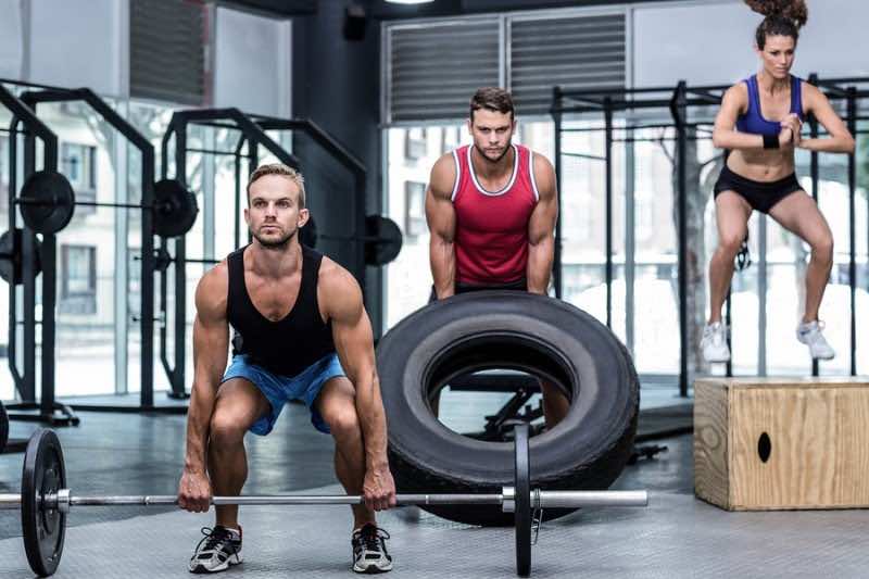 Three muscular athletes lifting and jumping at the crossfit gym