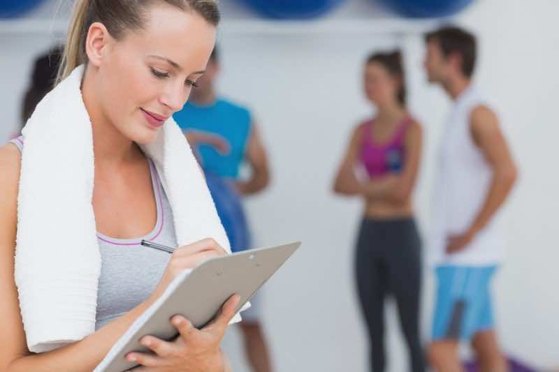 Female trainer writing on clipboard with fitness class in backgr