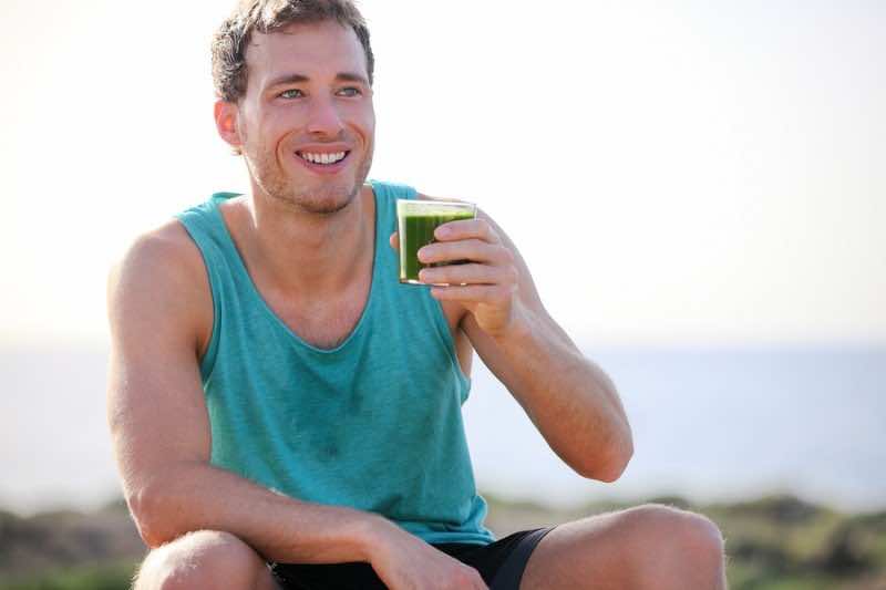 Green smoothie man drinking vegetable juice after running sport