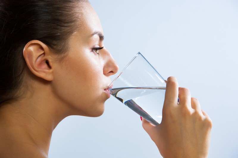 Close-up of pretty young woman drinking water from glass