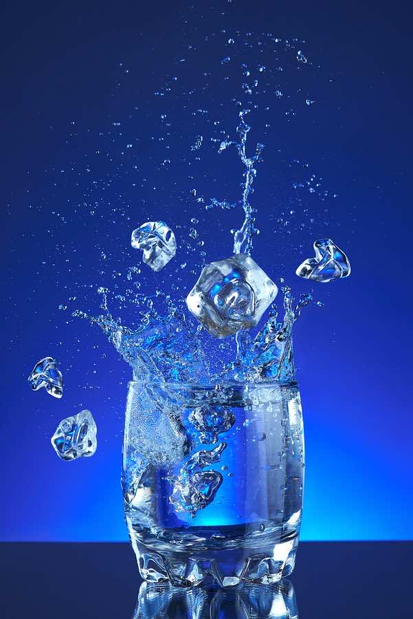 Water splash poured into a glass, blue background, refreshing, f