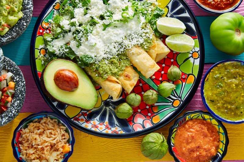 Green enchiladas Mexican food with guacamole and sauces on color