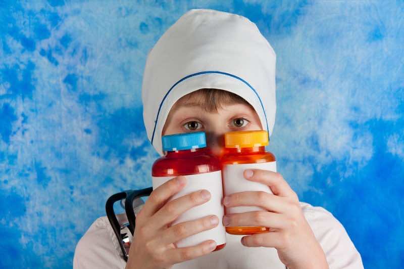 Boy in white doctor's costume and cap looking out two bottles for pills