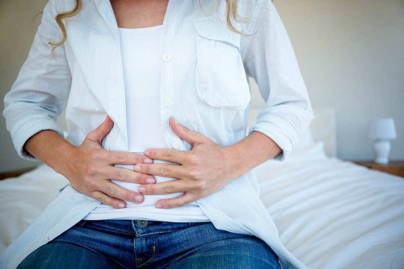 woman sitting on her bed clutching her stomach in discomfort