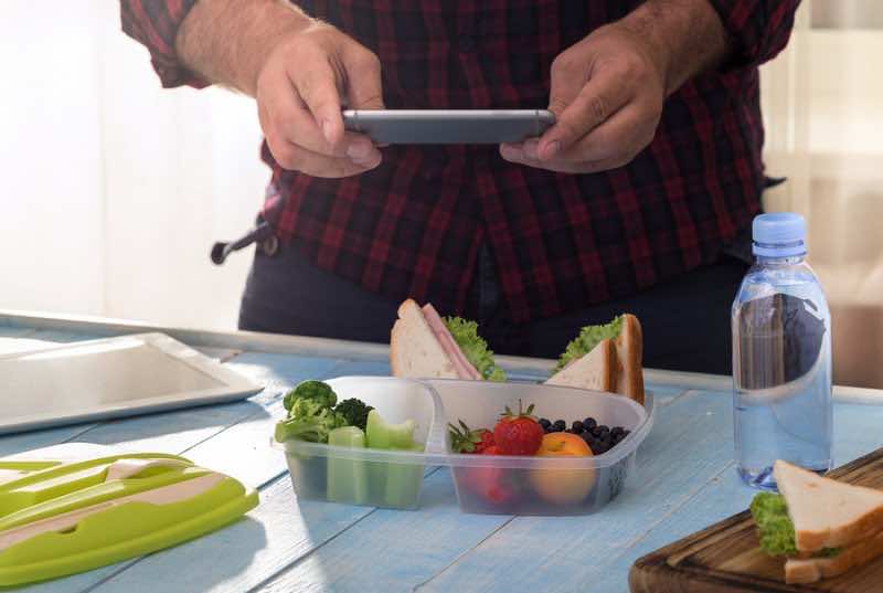 Man photographing lunch box with healthy food.
