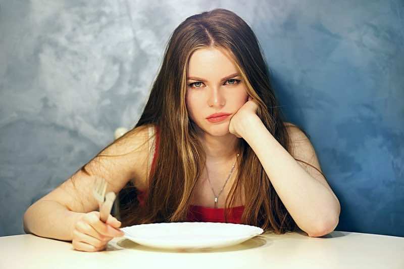 Hungry young woman waiting with an empty plate.